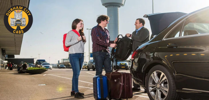 A friendly taxi driver loading luggage into the boot of a black car for a smiling couple at an airport.