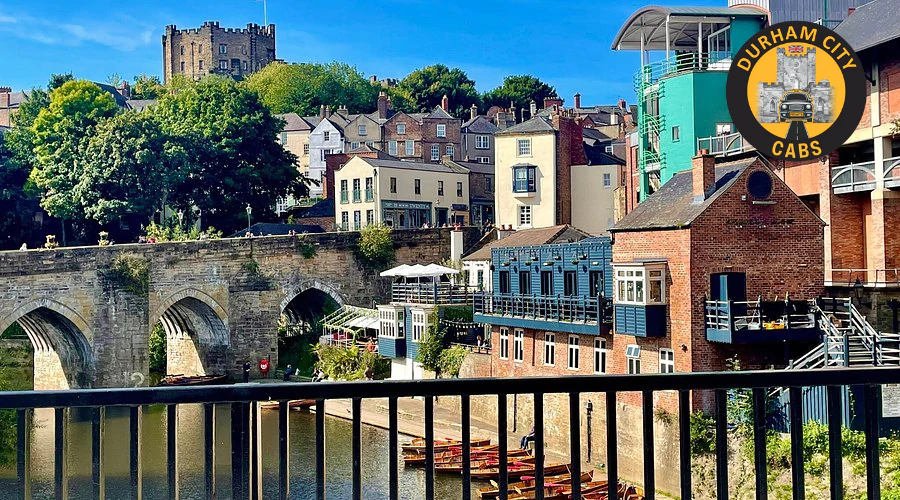 A picturesque view of the River Wear in Durham, with the historic stone arch of Elvet Bridge crossing it. Buildings with varying architectural styles line the riverbanks, including ones with teal and brick facades. Rowboats are visible on the water, and Durham Castle can be seen in the distance on a hill. The Durham City Cabs logo is in the top right.